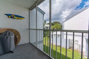 A balcony with a view of a backyard, a surfboard, and a sign on the wall.