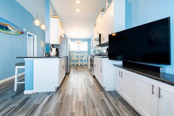A modern kitchen with white cabinets, a large TV, and a dining area with a table and chairs.