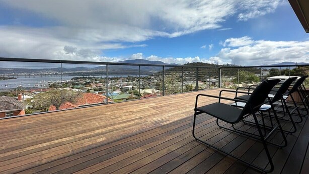 A wooden deck with metal chairs overlooking a cityscape and a body of water.