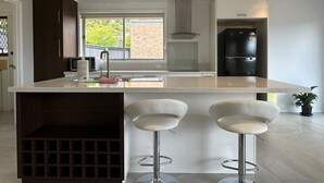 A modern kitchen with a central island, bar stools, a refrigerator, and a window with a view of greenery.