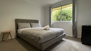 A bedroom with a bed, a small wooden stool, a black cabinet, and a window with curtains.