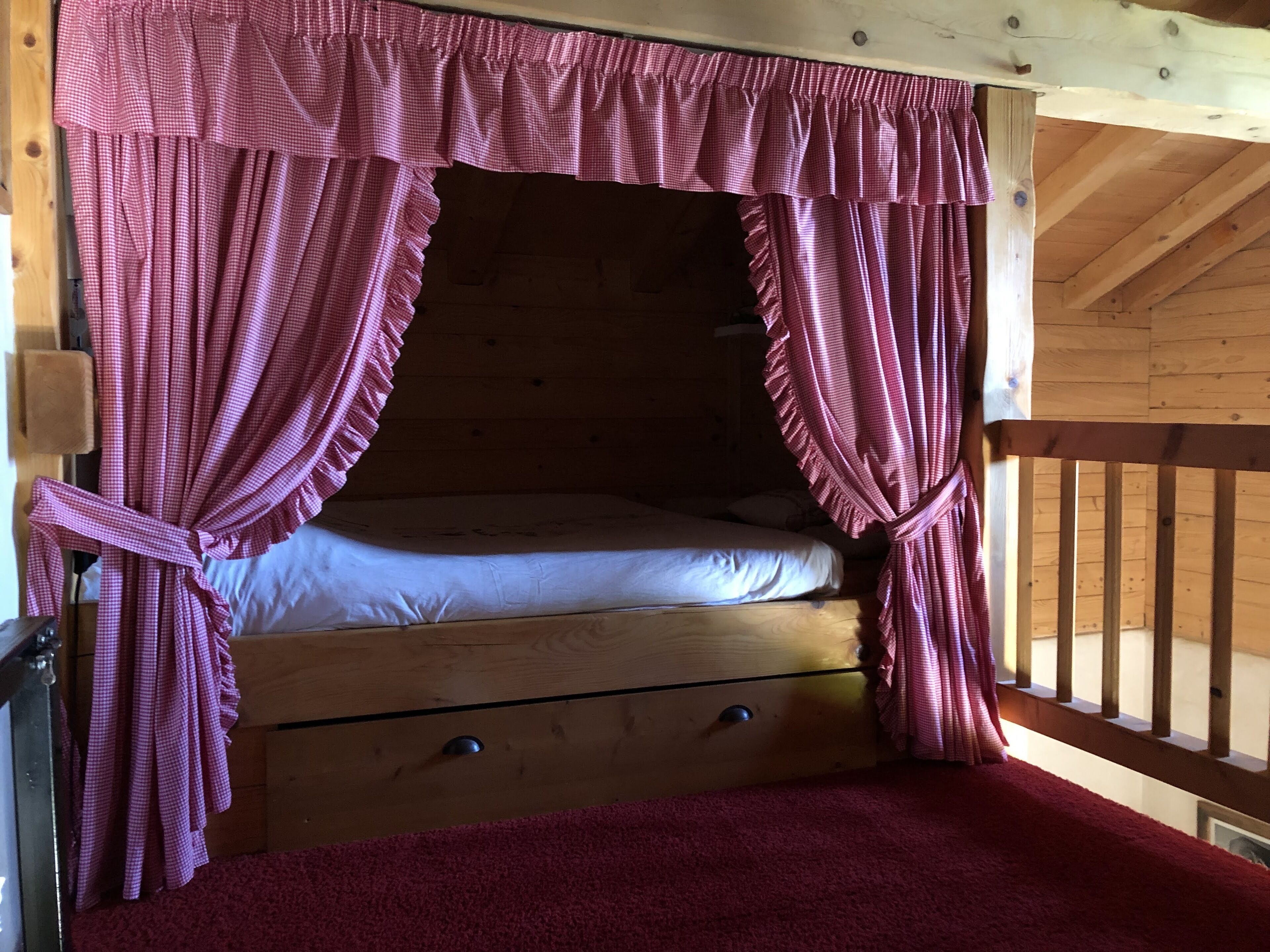 Une chambre dans un chalet en bois, avec un lit simple, une commode en bois et un tapis rouge.