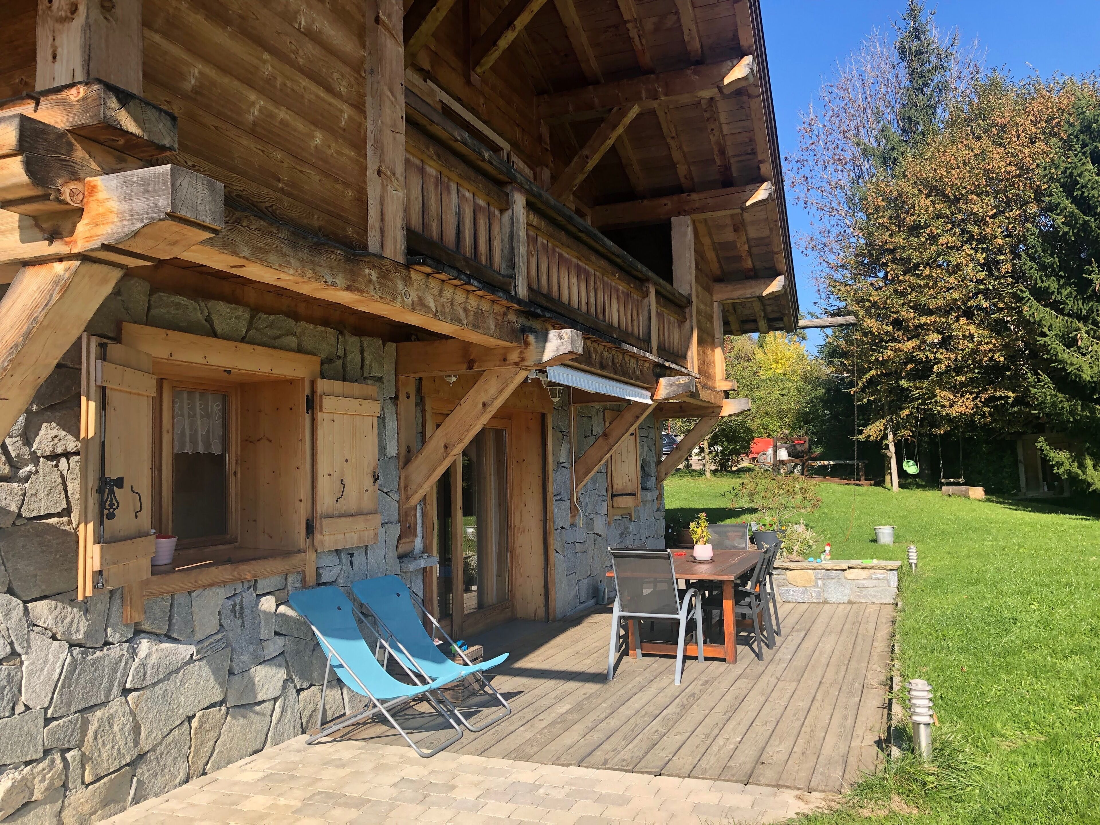 A wooden cabin with a stone foundation, a covered deck, and two blue lounge chairs.