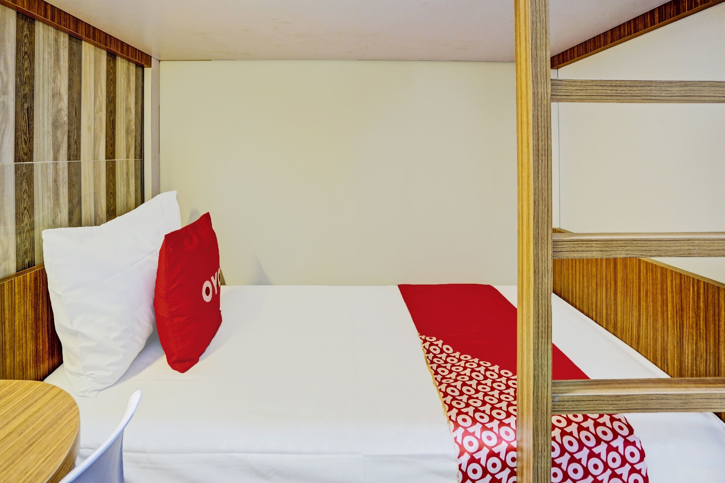A hotel room with a bed, a wooden headboard, a small round table, and a red and white patterned throw blanket.