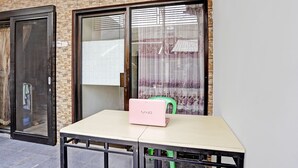 Une table avec un ordinateur portable et une chaise, placées à l’extérieur, devant un bâtiment à la façade en briques et aux grandes fenêtres.