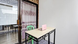 Une pièce avec une table, un ordinateur portable, une chaise verte et une fenêtre avec des rideaux.