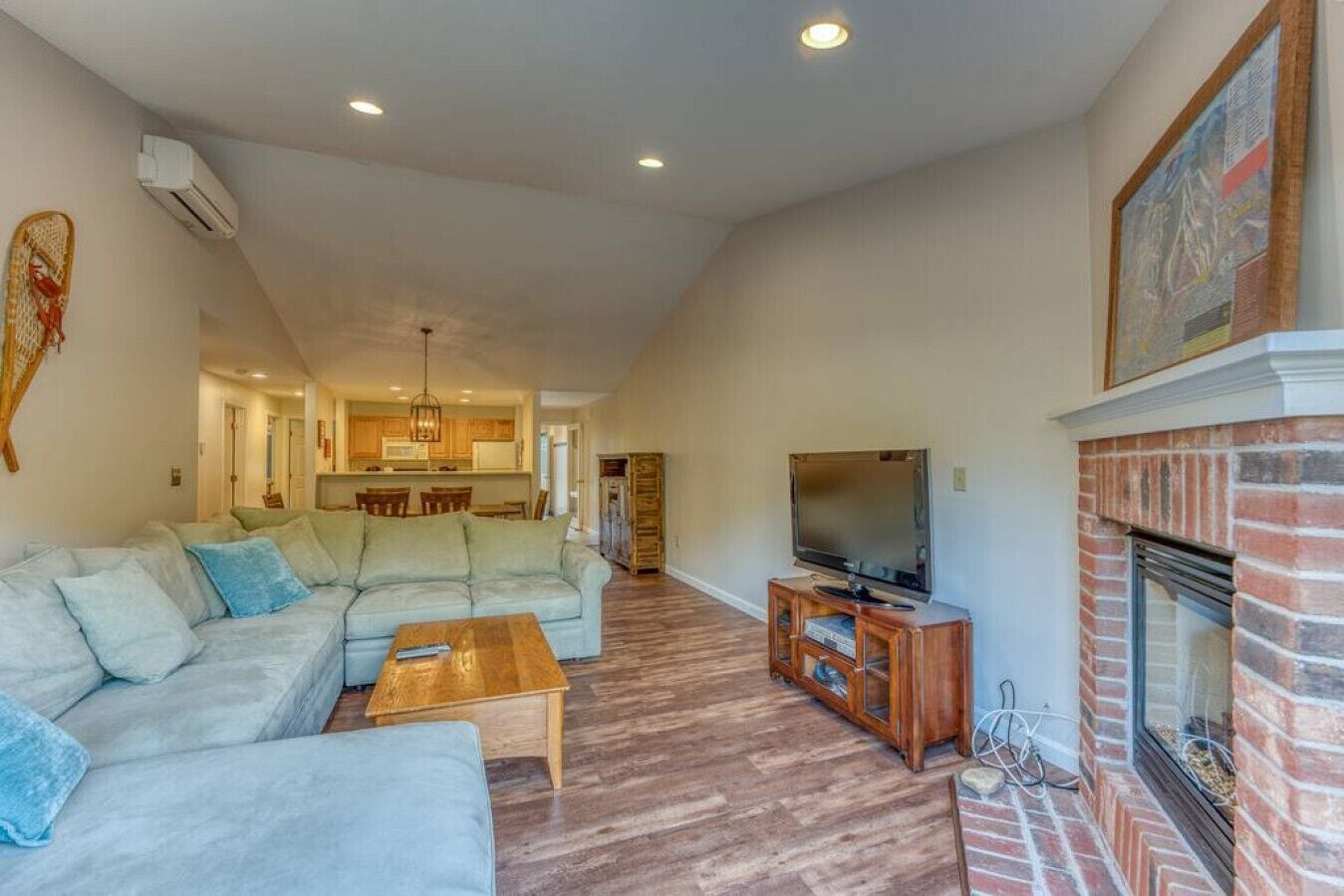 A spacious living room with a sectional sofa, a coffee table, a TV on a wooden stand, and a fireplace.