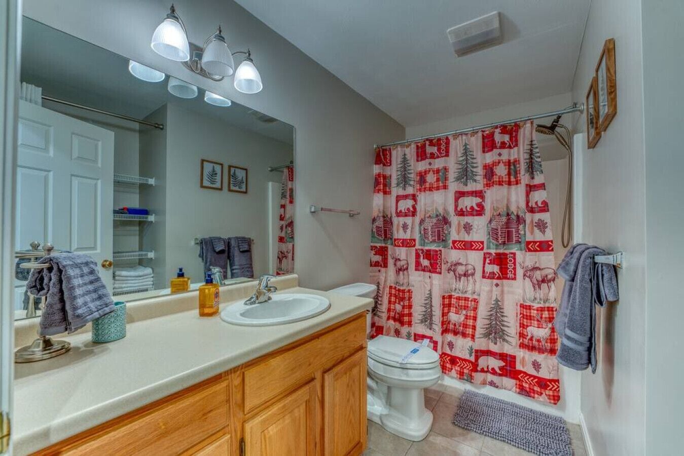 A bathroom with a double sink, wooden cabinets, a mirror, and a shower curtain with a forest and animal pattern.