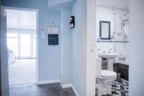 Un baño con inodoro, lavabo y ducha. Hay un letrero de bienvenida en la pared y un extintor.