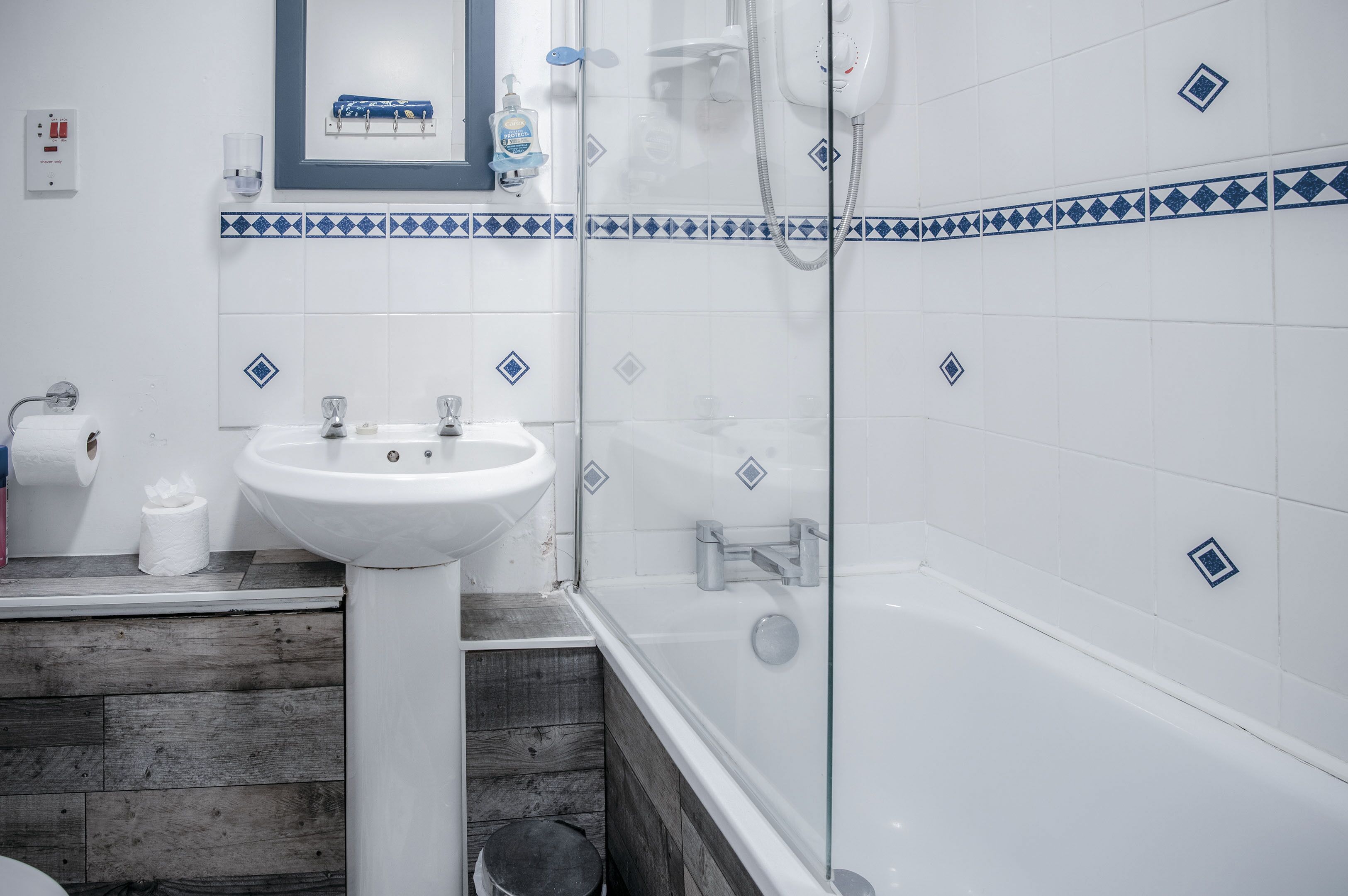 Une salle de bain avec un lavabo blanc, une cabine de douche en verre et un plancher en bois.