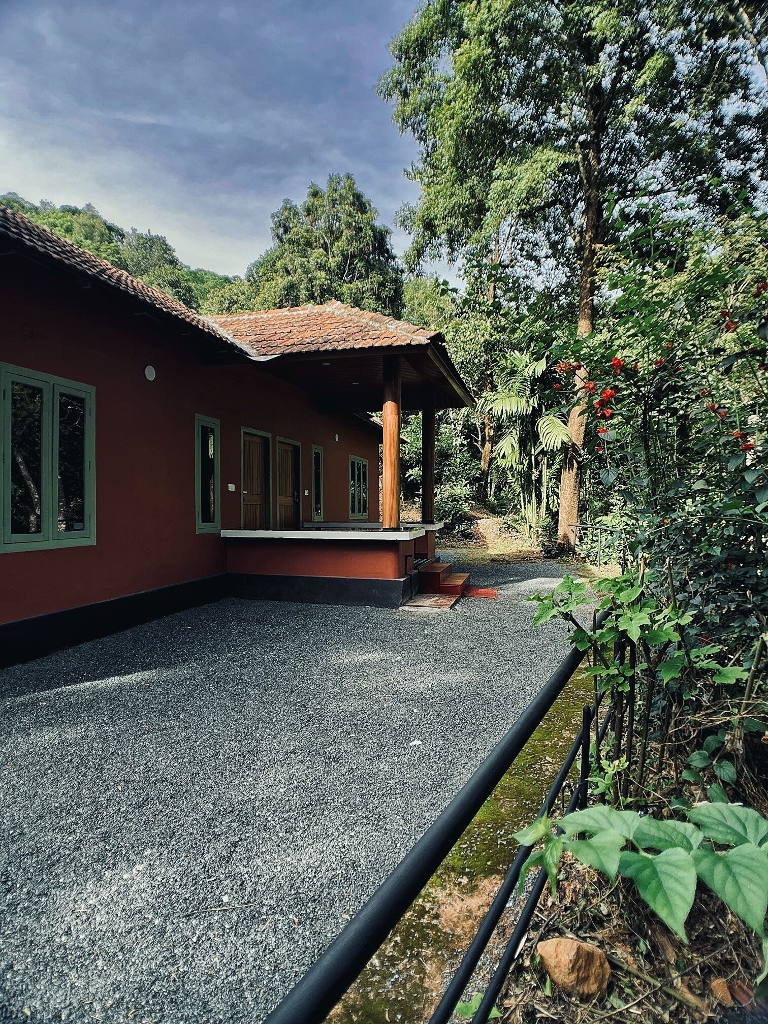 A house with a red exterior and a tiled roof, surrounded by gravel and greenery.