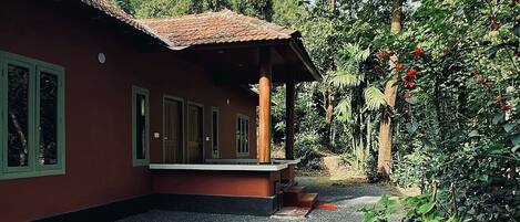 A house with a red exterior and a tiled roof, surrounded by gravel and greenery.