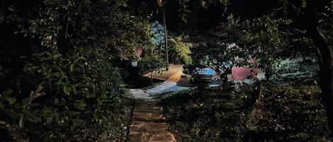 A stone pathway leading through a garden at night with a building in the background.