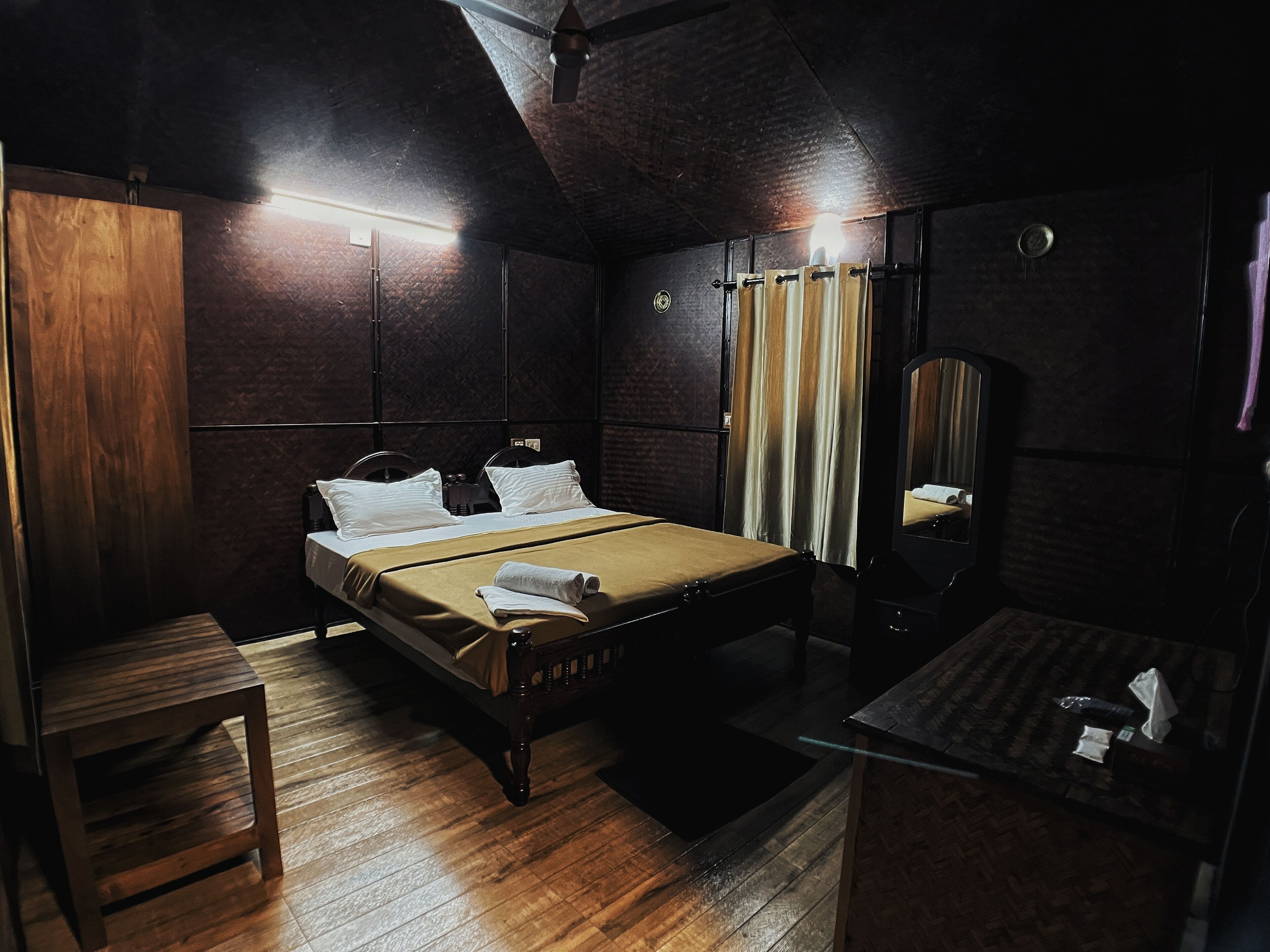 Una habitación con poca luz, una cama de madera, una mesita y un espejo.