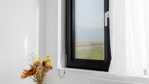 A room with a large window, a white radiator, and a vase with flowers on a white table.