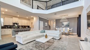 Un vaste espace de vie comprenant un grand canapé d’angle blanc, une table basse et un coin repas avec une table et des chaises blanches.