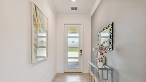 Un couloir avec une porte en verre, une console ornée d’objets décoratifs et un grand tableau abstrait accroché au mur.