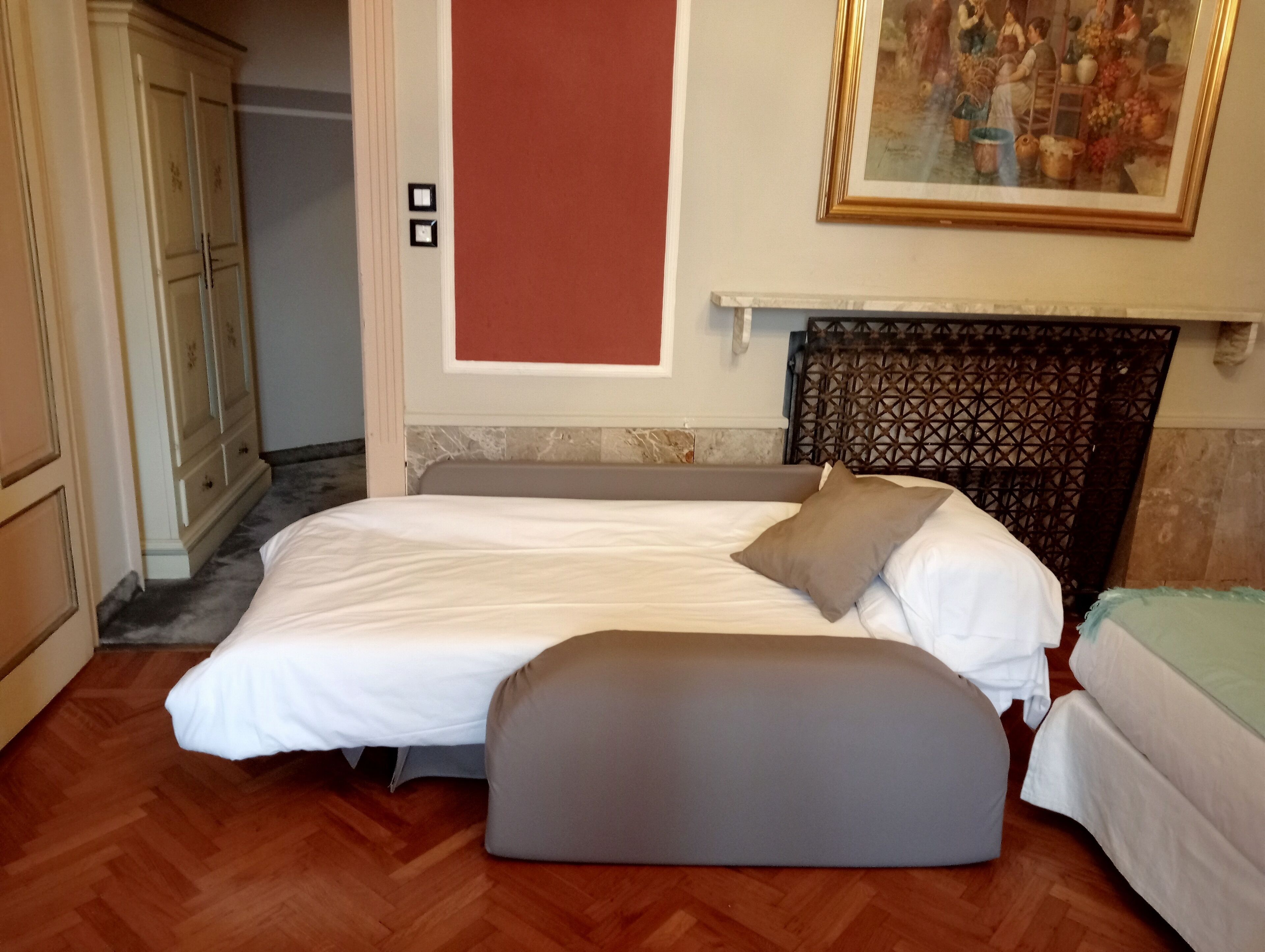 A bedroom with a bed, a bench, a wardrobe, and a painting on the wall.