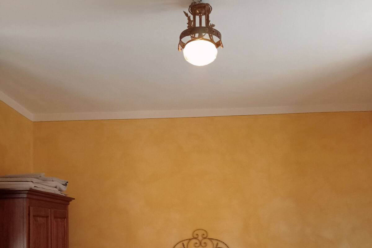A bedroom with a bed, two bedside tables, a wooden wardrobe, and a decorative ceiling light fixture.