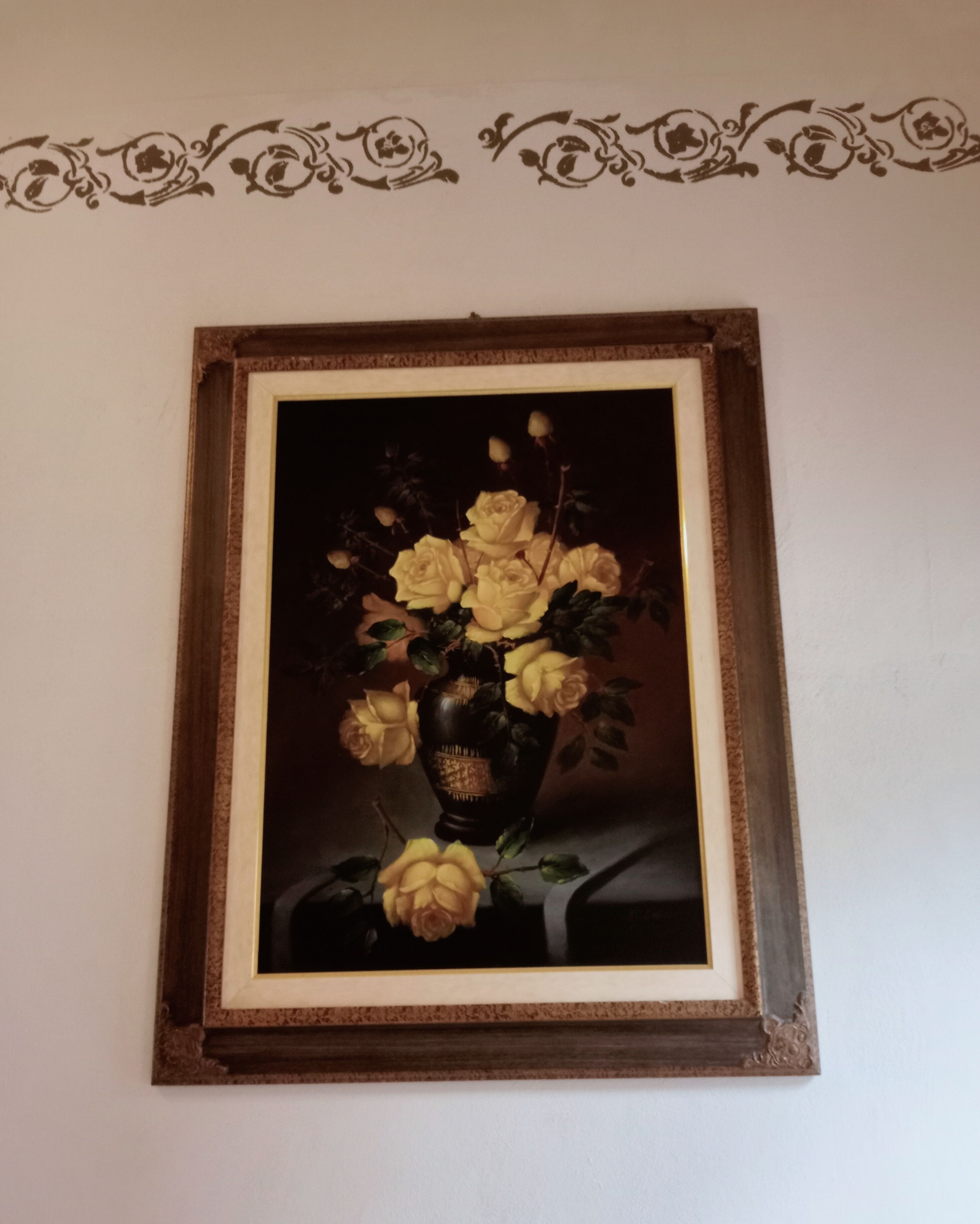 A framed painting of yellow roses in a dark vase on a table.