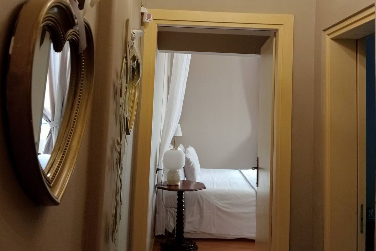 A hallway leading to a bedroom with a bed, a chandelier, and a mirror on the wall.