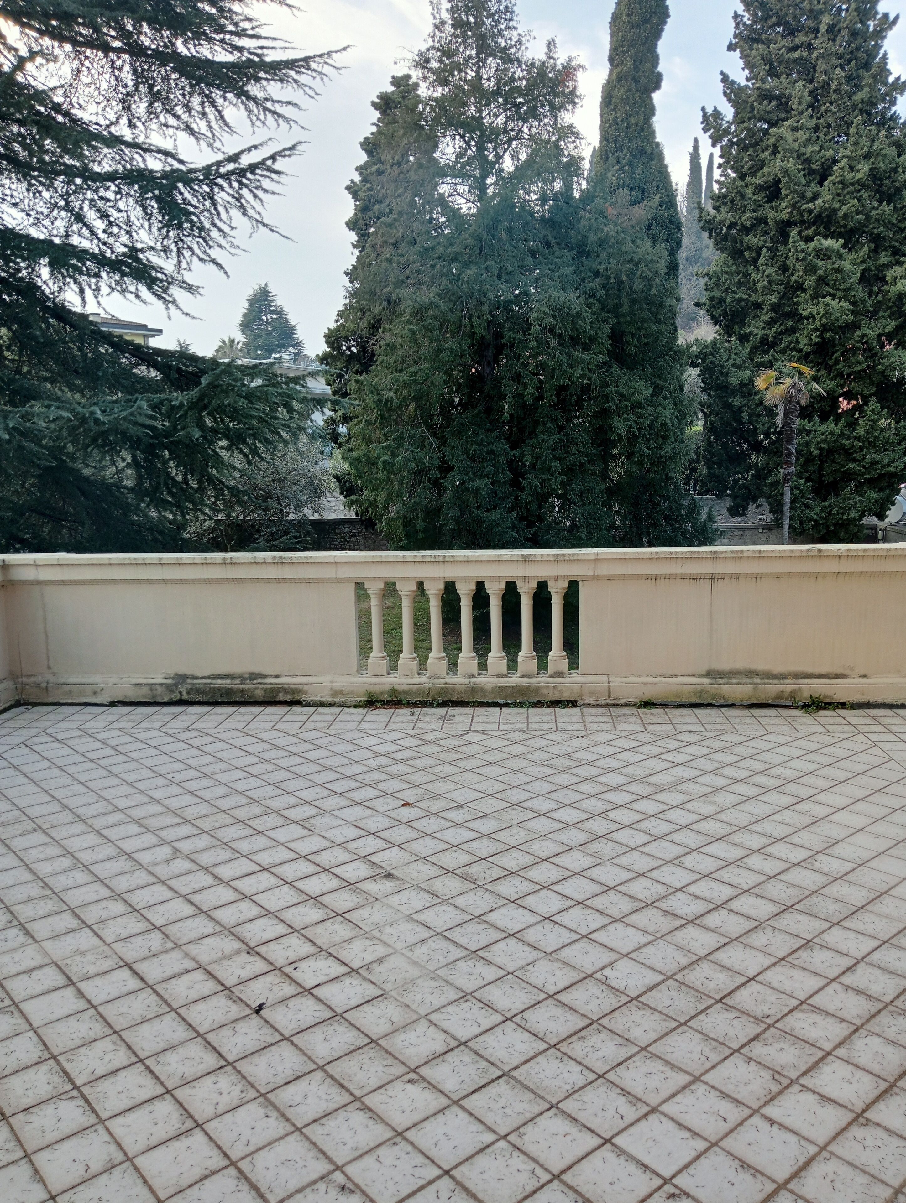 Terraza con baldosas, barandilla y vista a árboles altos.