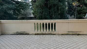Terraza con baldosas, barandilla y vista a árboles altos.