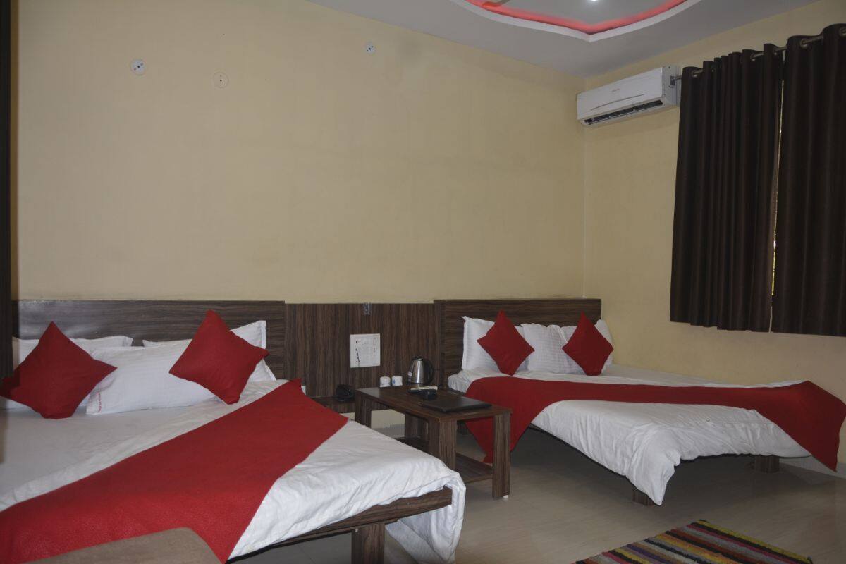A hotel room with two beds, each with red and white bedding, a small wooden table, and an air conditioning unit on the wall.