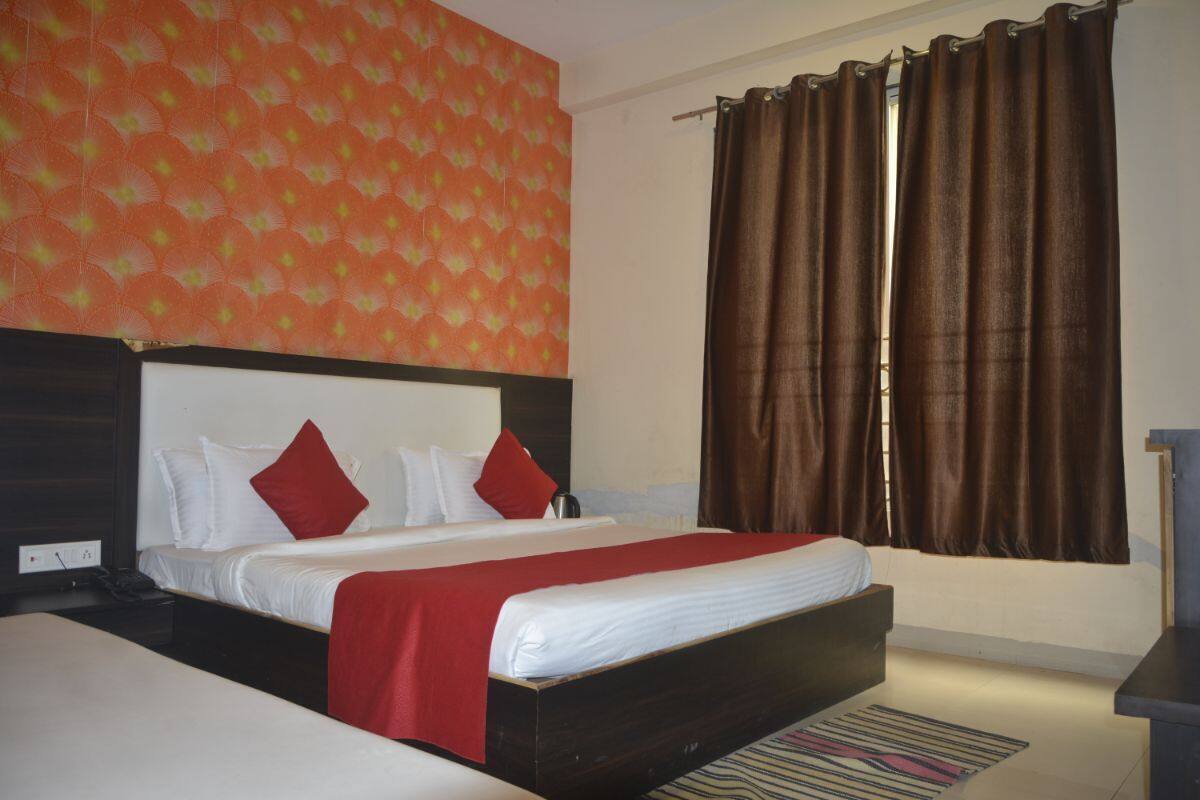 A hotel room with a large bed, a headboard, a window with curtains, and a patterned wall.