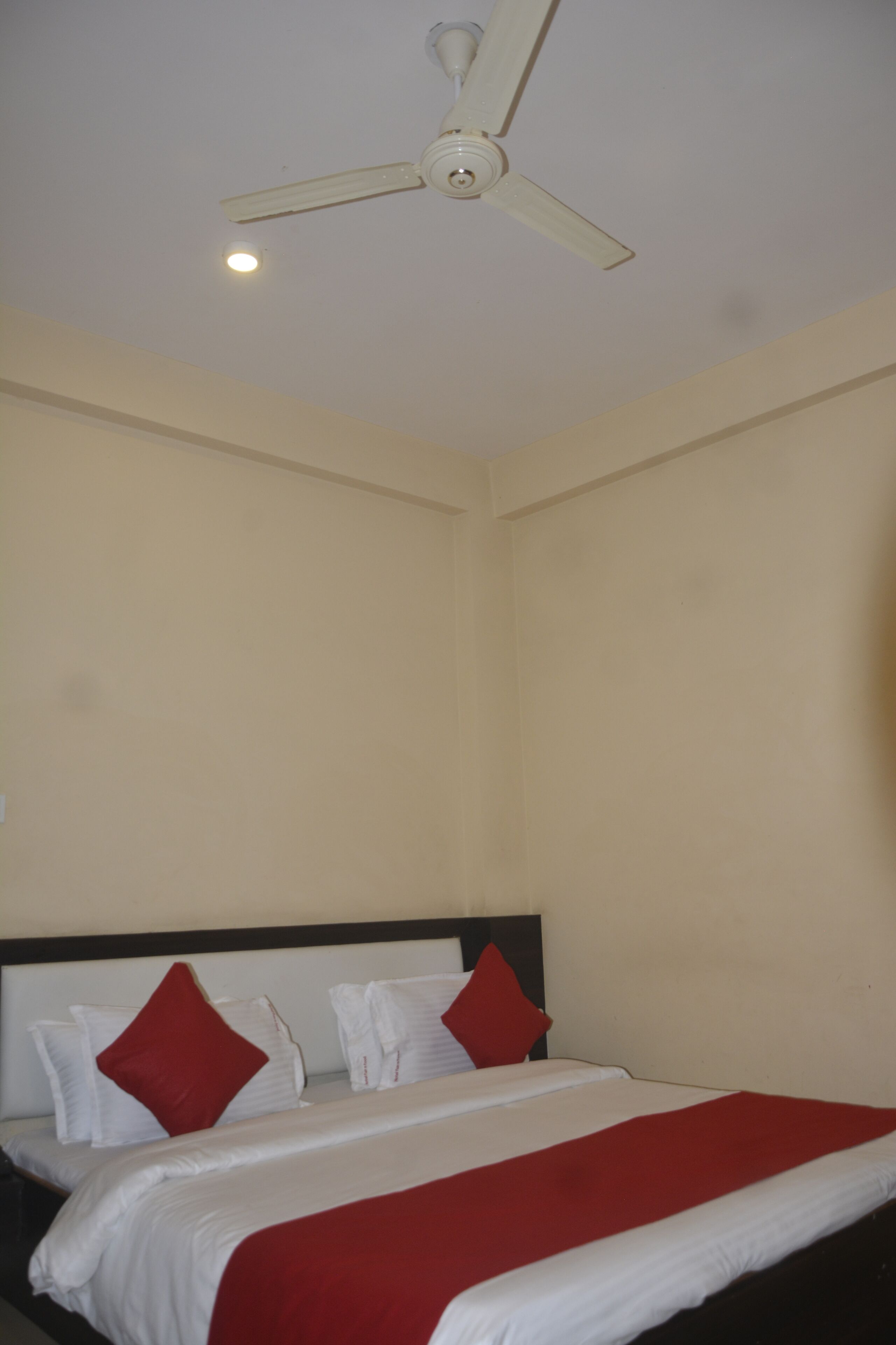 Una camera d'albergo con un letto, biancheria bianca, cuscini rossi, una ventola a soffitto e un lampadario.
