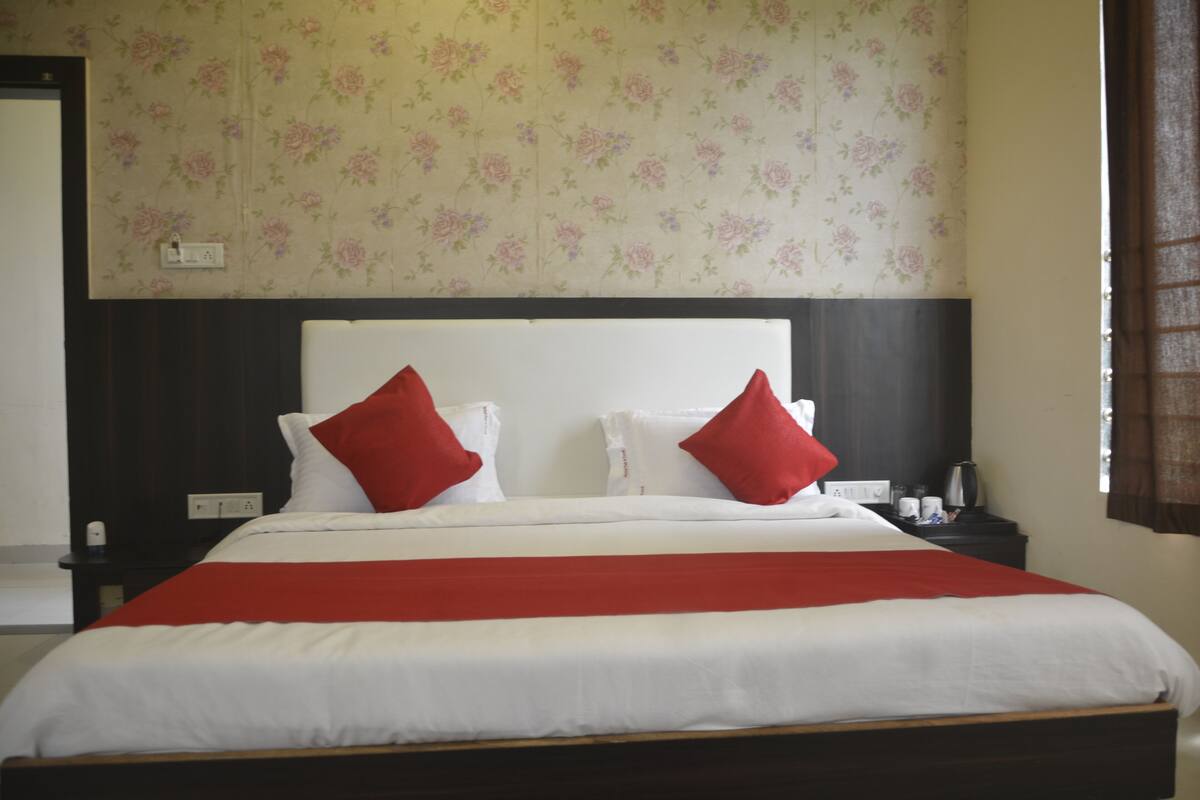 A neatly made bed with white and red bedding, a dark headboard, and floral wallpaper.