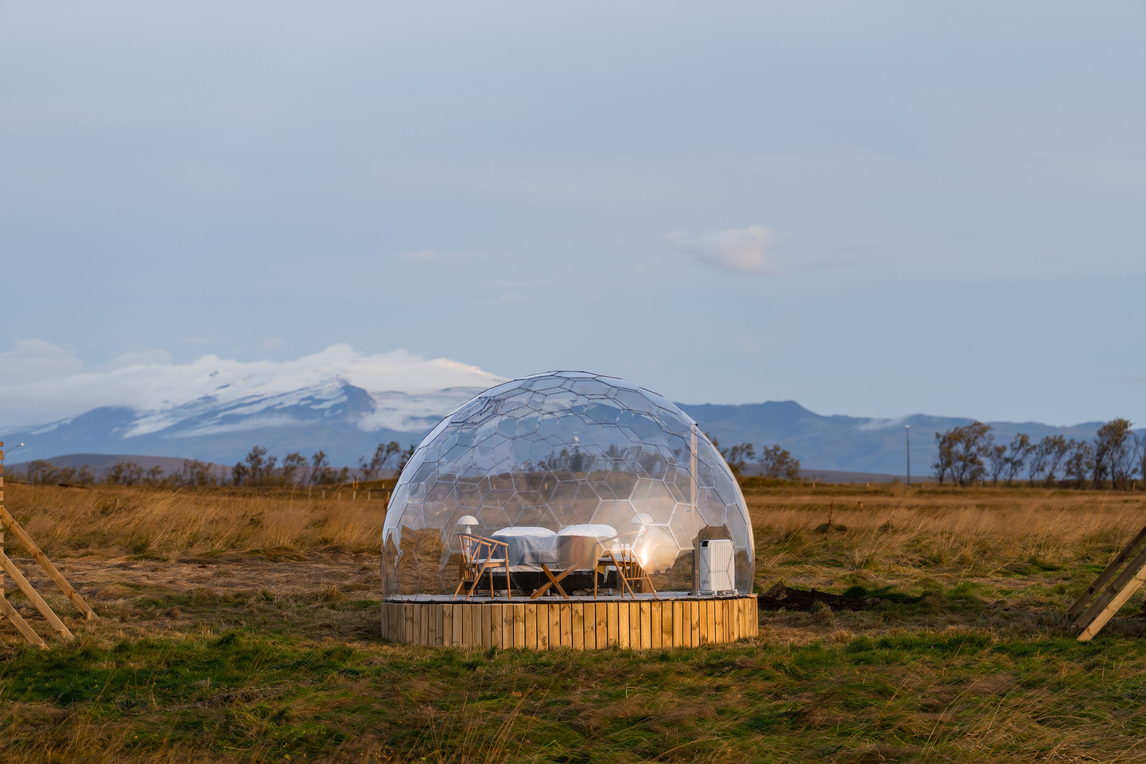 A geodesic dome structure with a wooden platform, a table, chairs, and a heater.