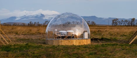 A geodesic dome structure with a wooden platform, a table, chairs, and a heater.