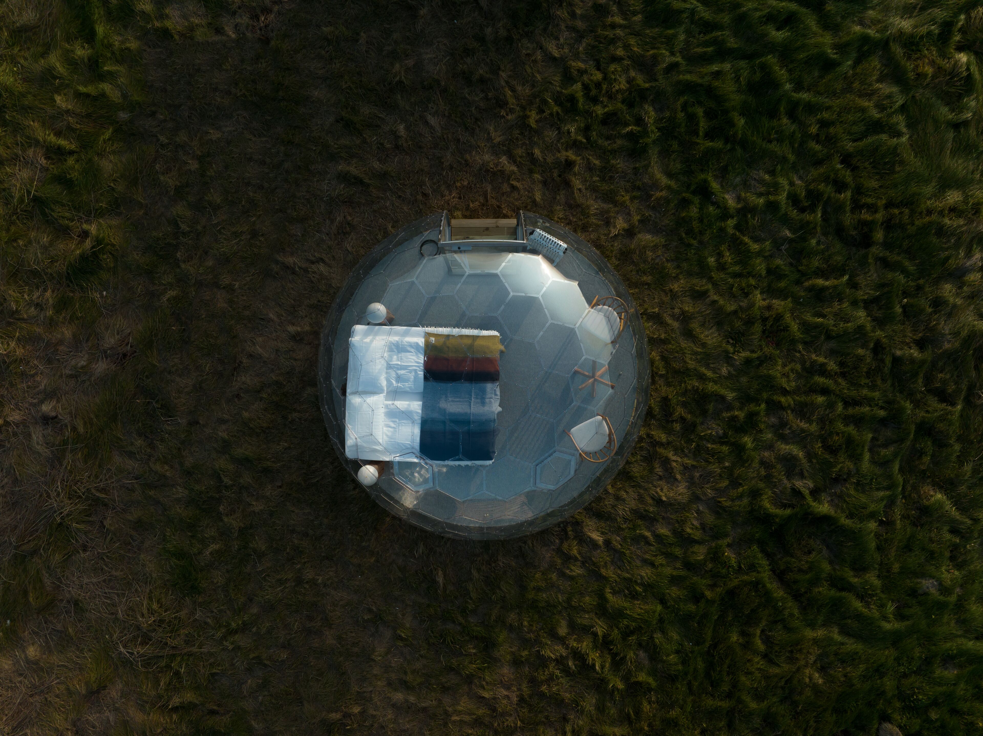 An aerial view of a round, transparent structure with a hexagonal pattern, surrounded by grass.