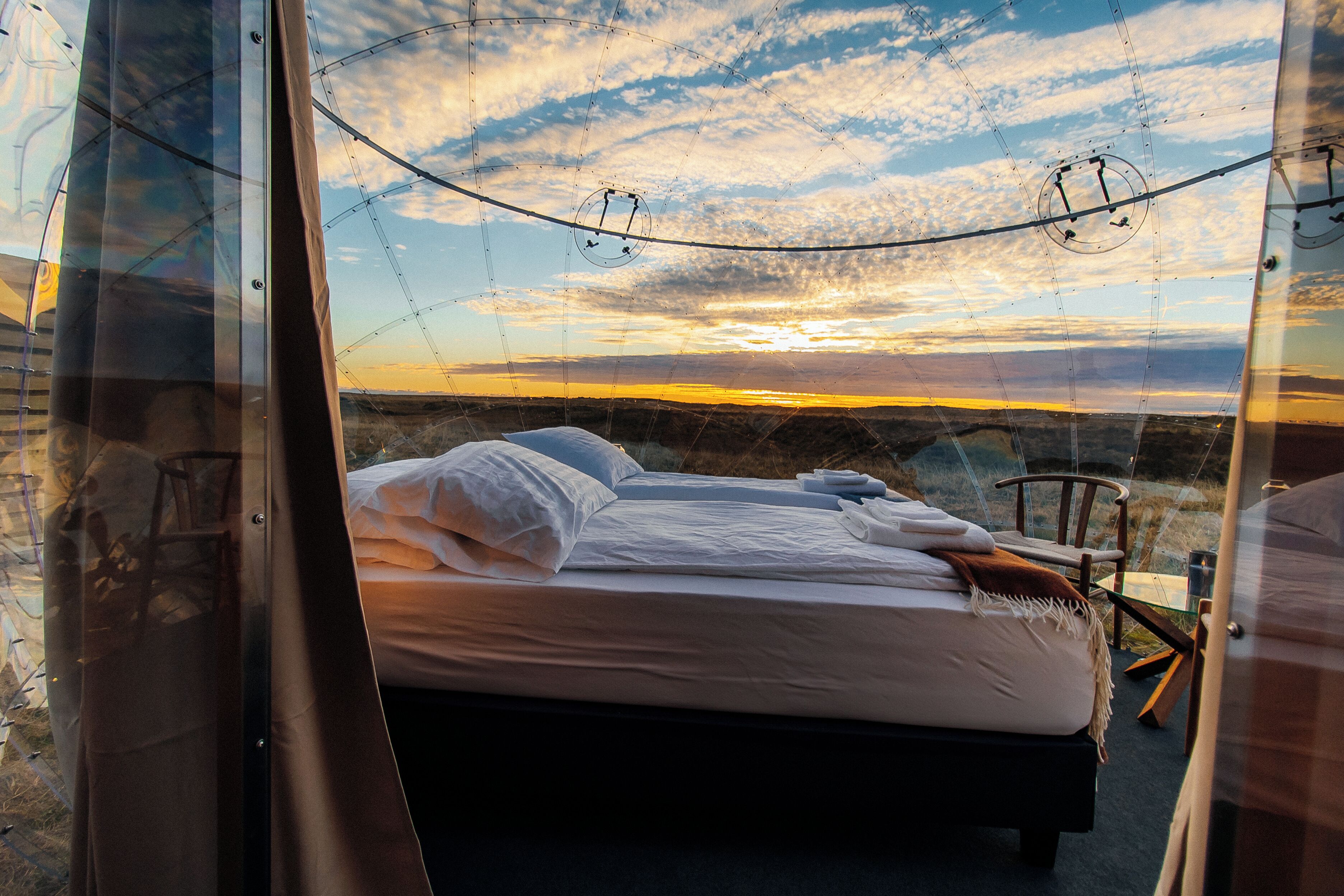 Una habitación con una cama, una silla y vista al atardecer.