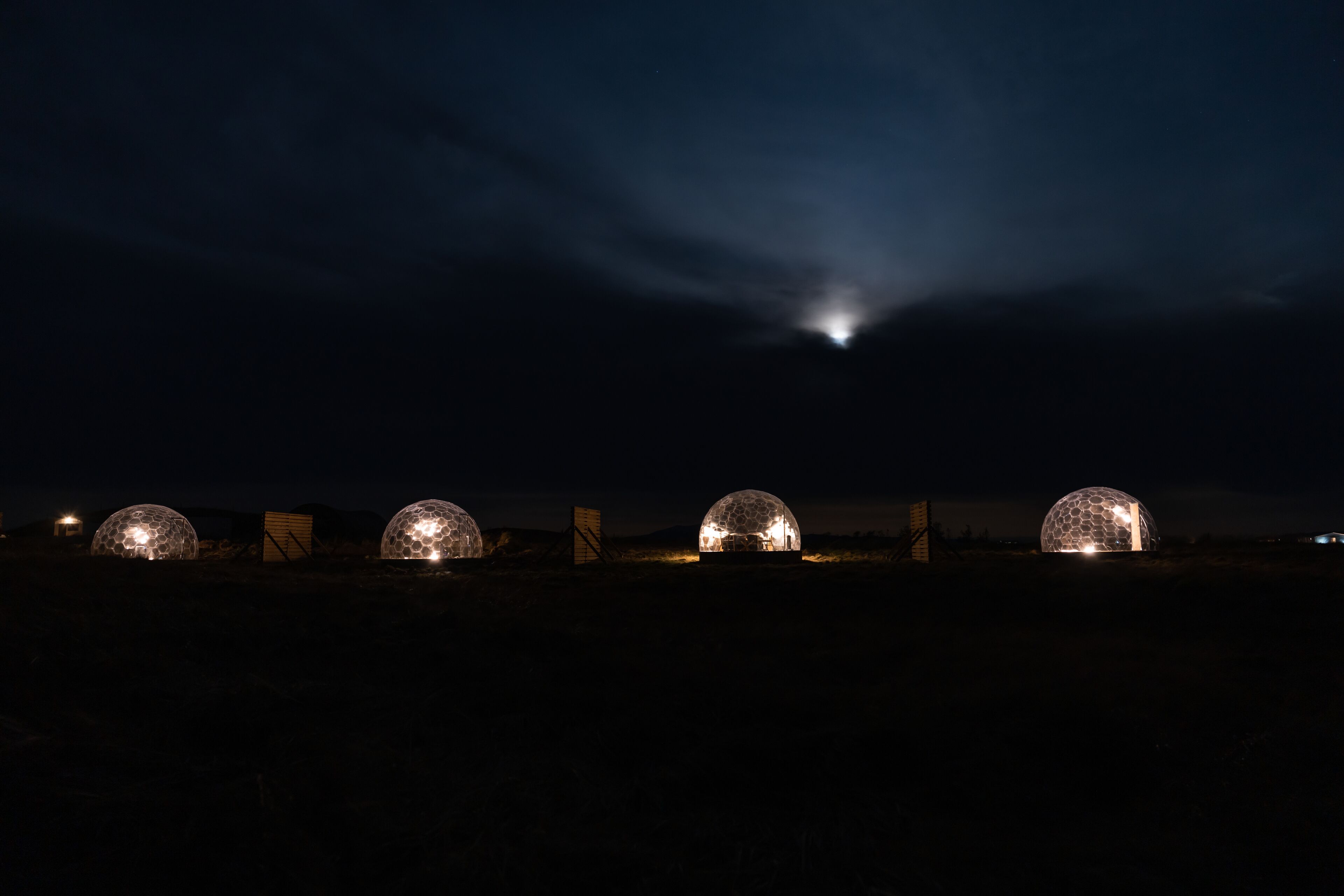 Four dome-shaped structures illuminated at night, likely accommodations, with a clear sky above.