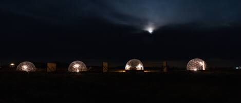 Four dome-shaped structures illuminated at night, likely accommodations, with a clear sky above.