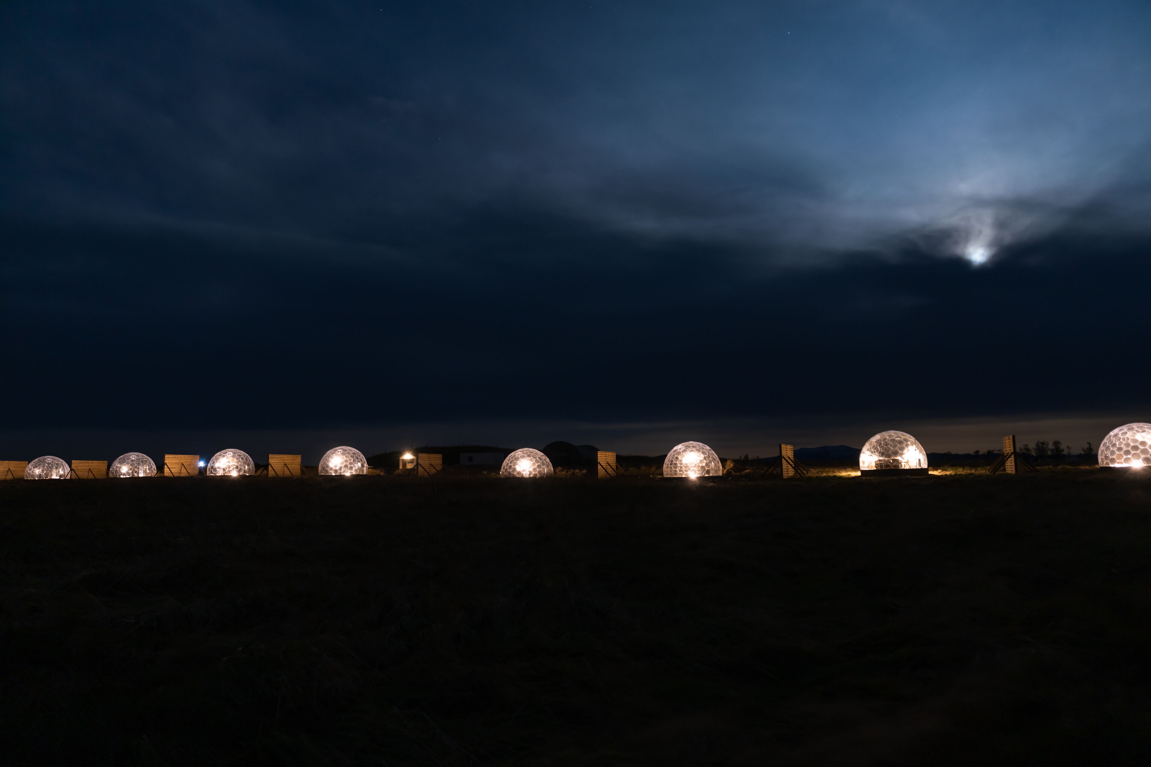 Een rij bolvormige constructies met verlichting, voor een donkere hemel met een zichtbare maan.