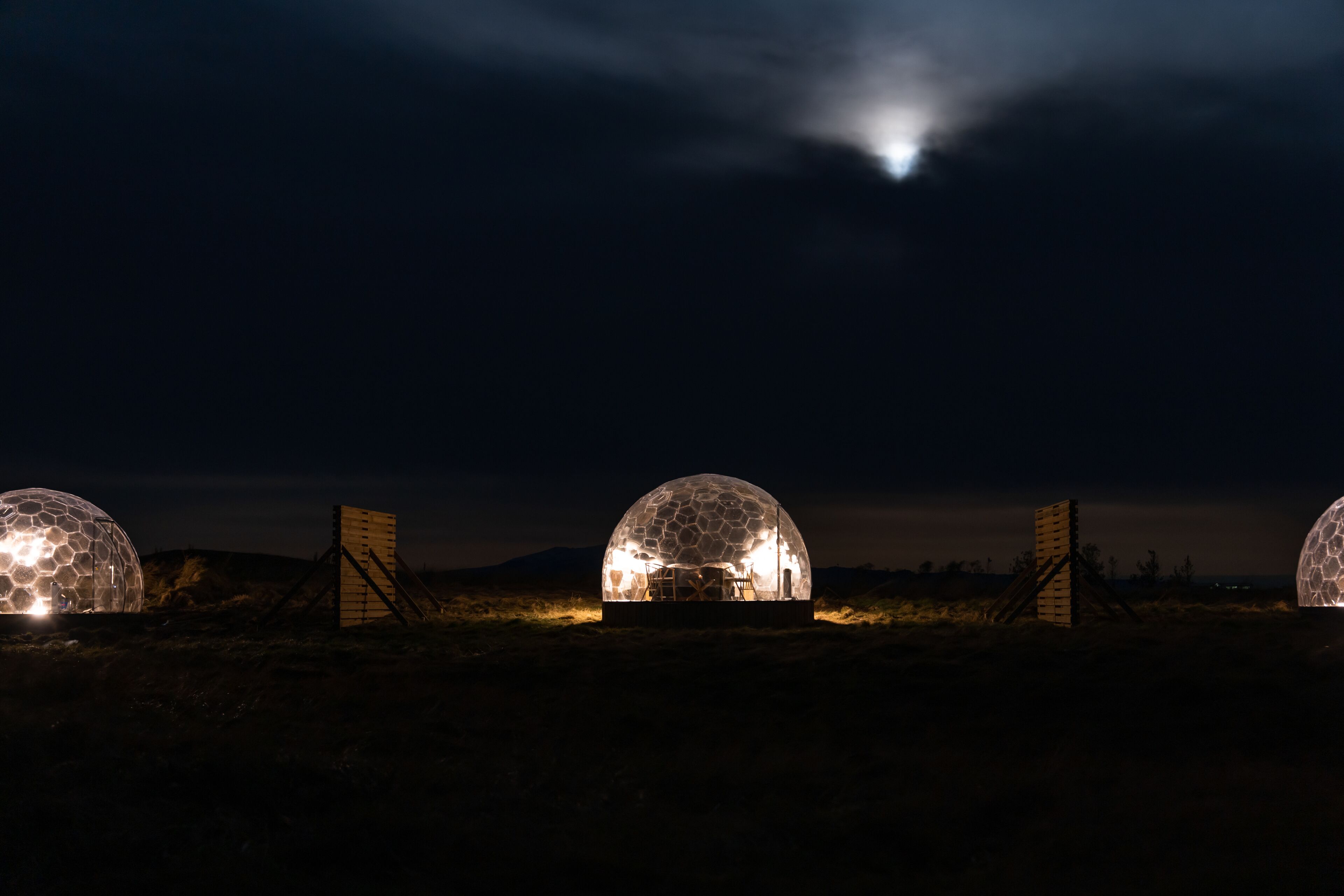 Three dome-shaped structures with interior lighting, set in a desert landscape at night.