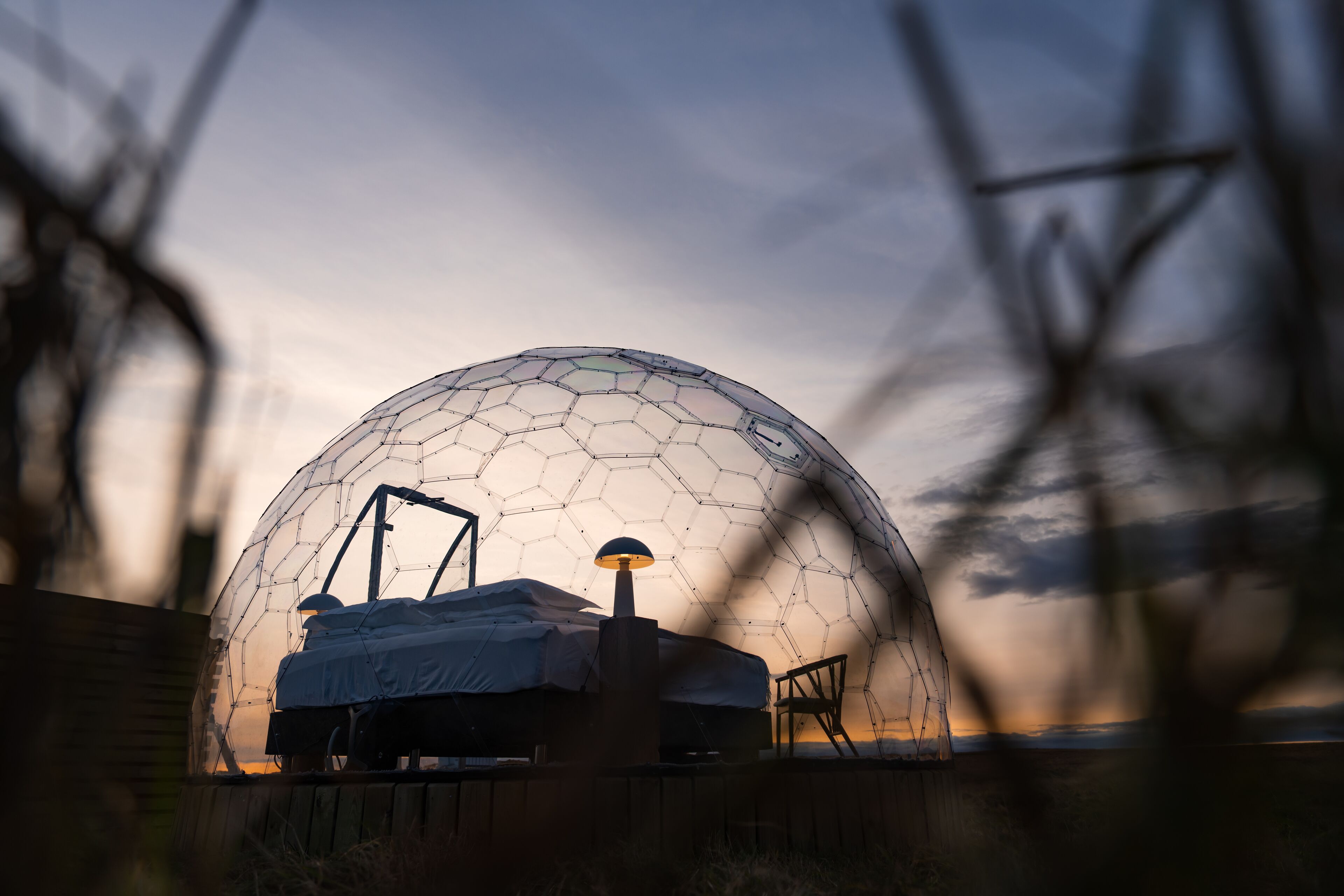 A dome-shaped structure with a bed and a lamp inside, surrounded by a wooden fence.