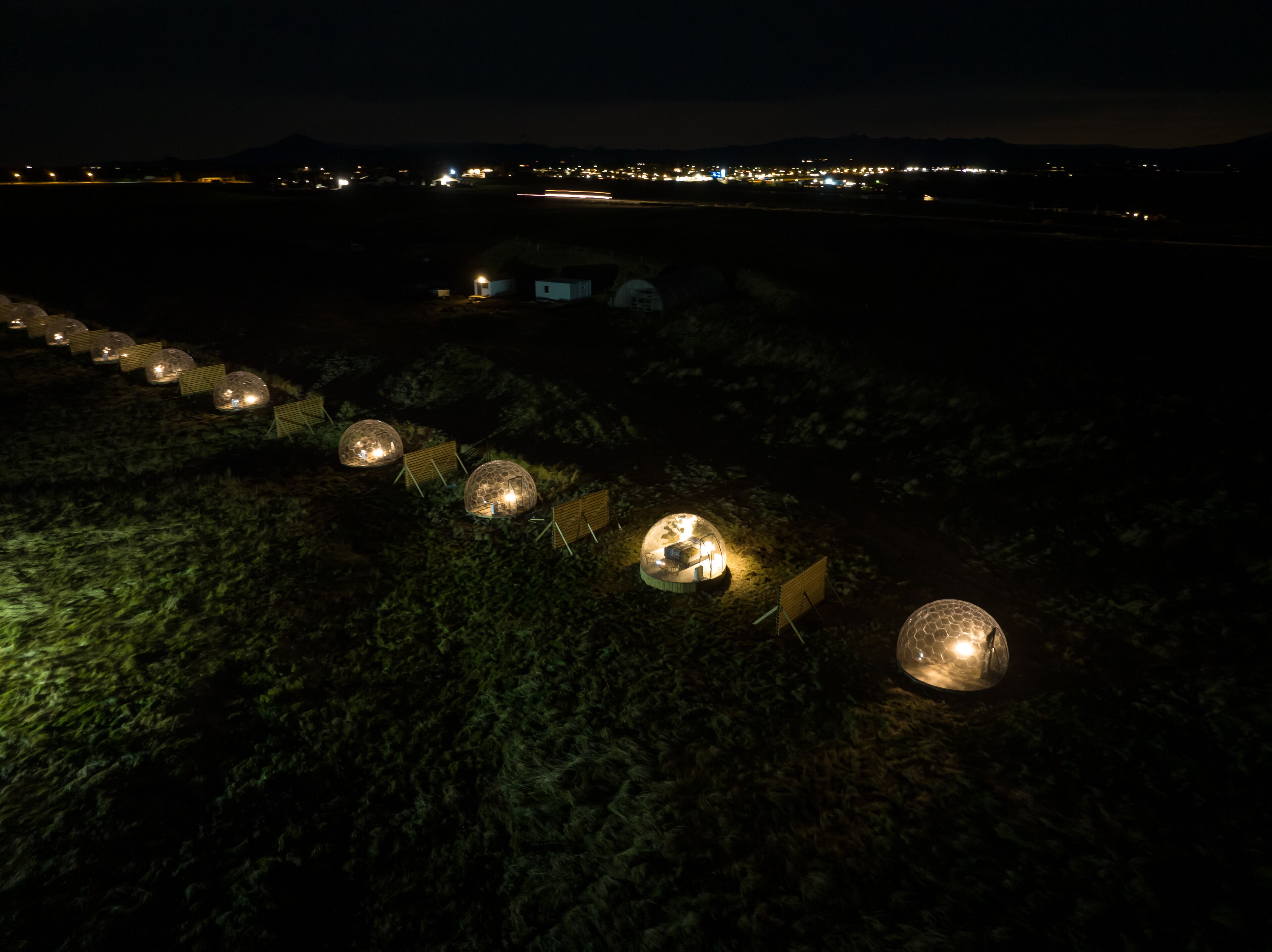 Une rangée de structures sphériques illuminées, installées dans un environnement naturel, de nuit.