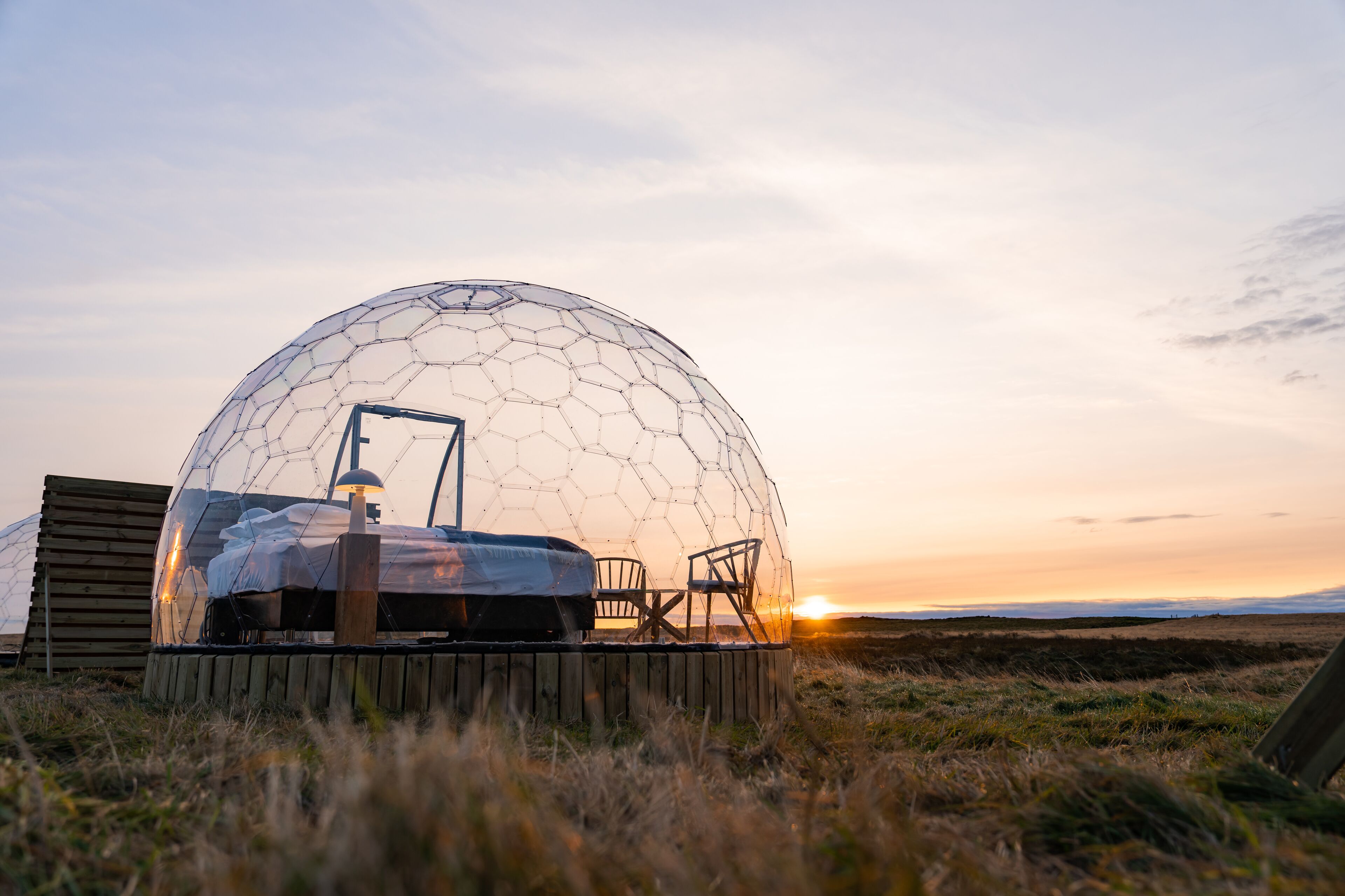 Uma estrutura em cúpula geodésica com deck de madeira, uma mesa e cadeiras.