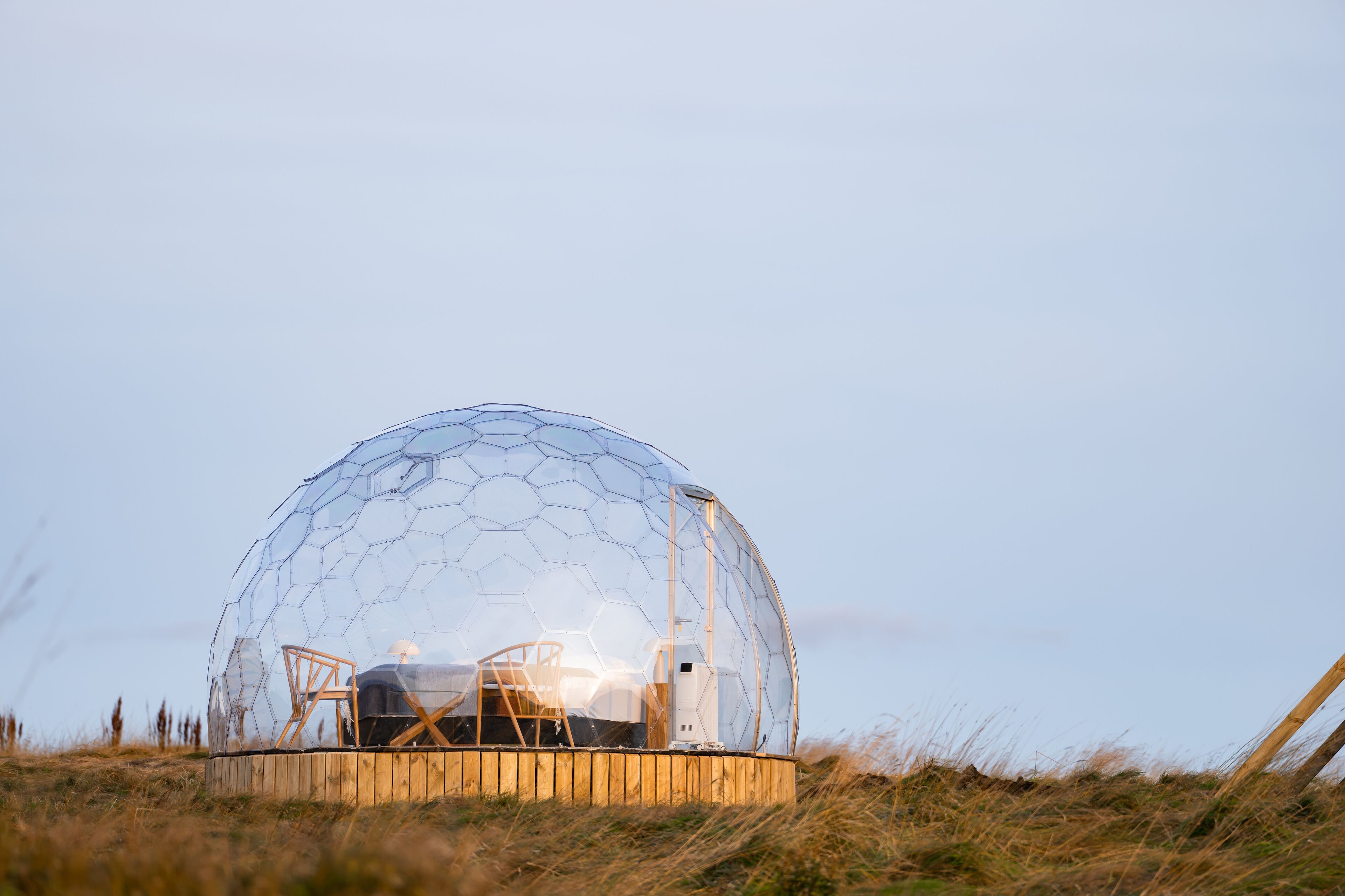A geodesic dome structure with a wooden platform and a bed inside.