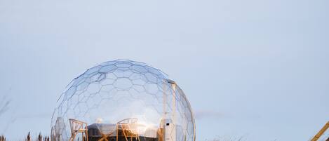 A geodesic dome structure with a wooden platform and a bed inside.