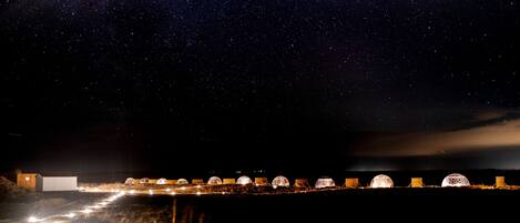 A series of dome-shaped tents illuminated at night, set against a starry sky.