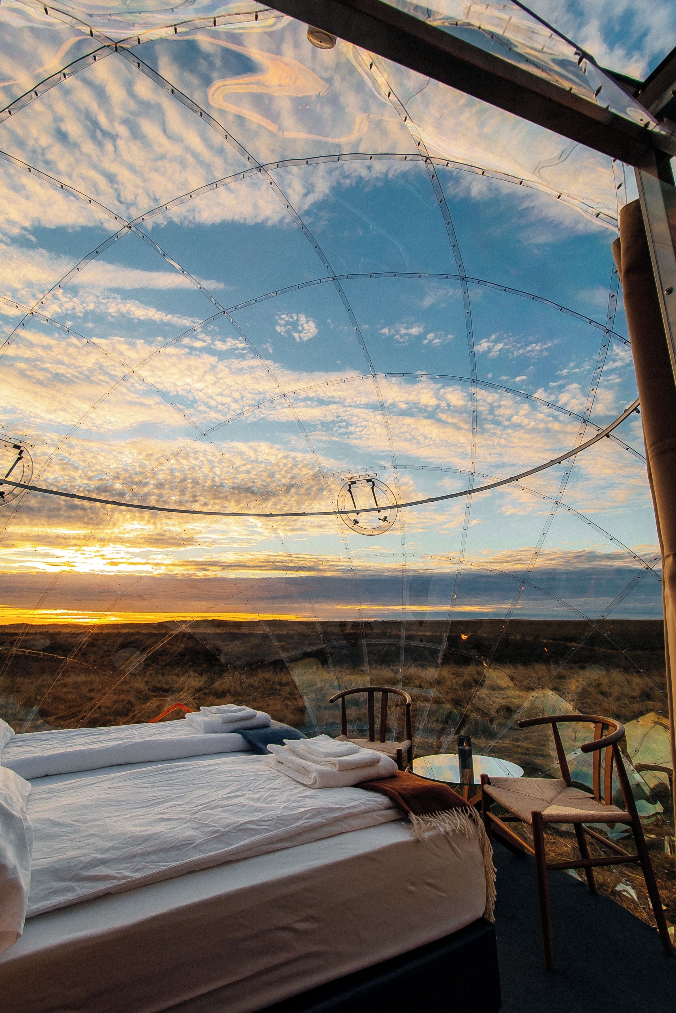 Ein Schlafzimmer mit Bett, Stühlen und Blick auf den Sonnenuntergang durch eine Glaskuppel.
