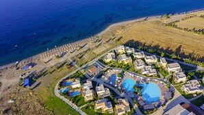 An aerial view of a coastal resort with multiple swimming pools, beachfront umbrellas, and a mix of residential and commercial buildings. - Natura Park Village Hotel & Spa  (Kos)