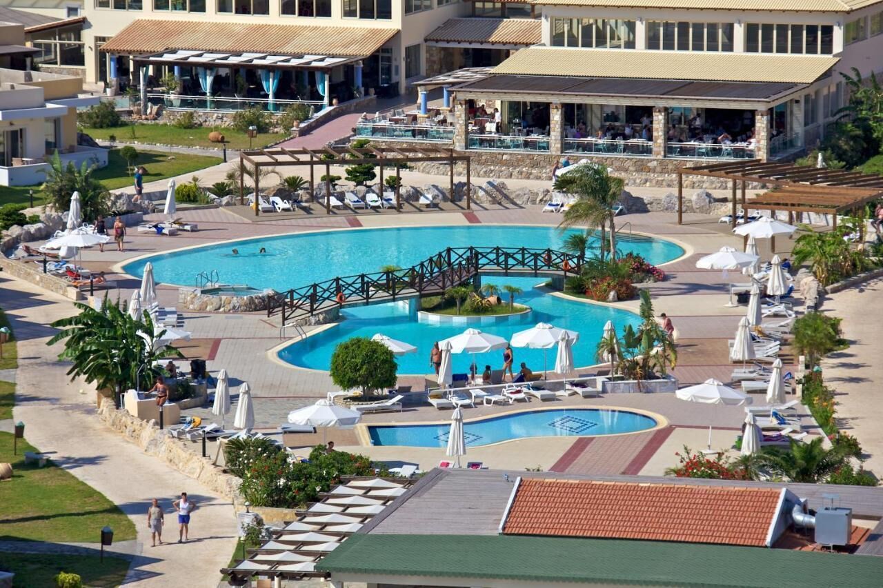 Un resort con una amplia piscina central, zonas de estar al aire libre y un bar/salón cubierto.