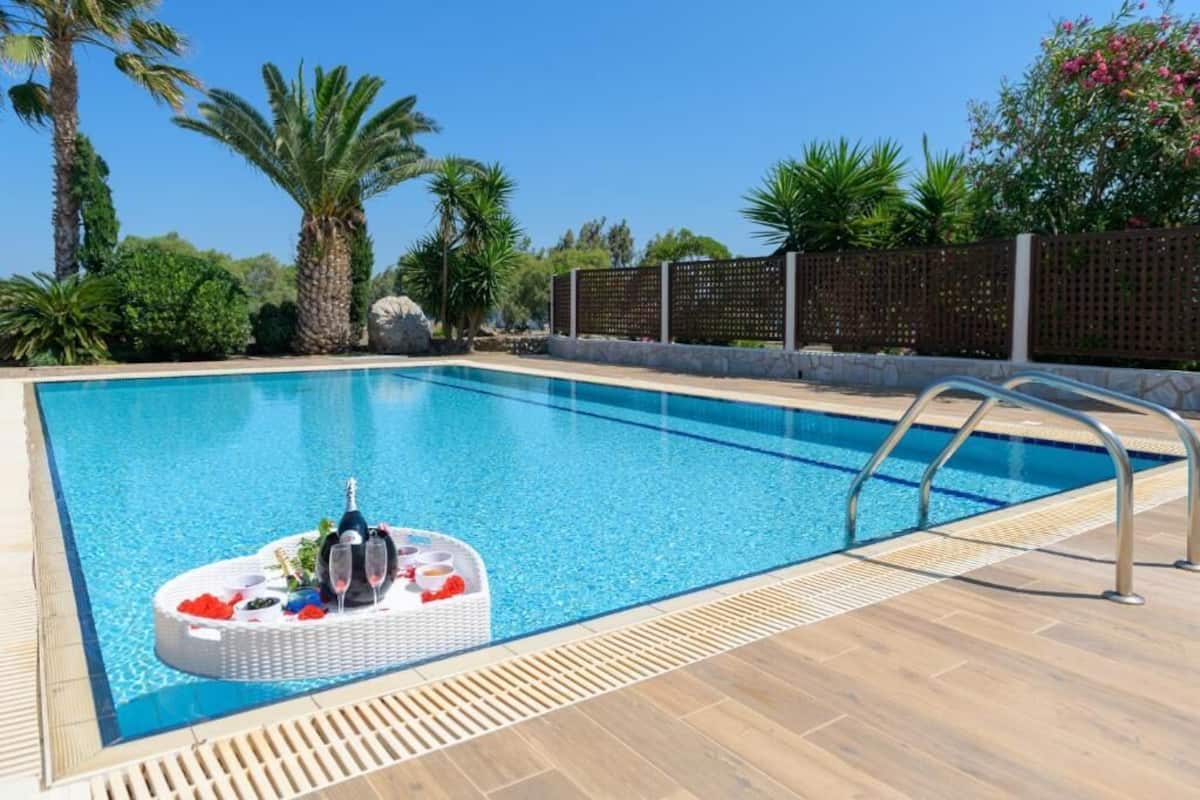A swimming pool with a floating bar area, surrounded by palm trees and a wooden deck.
