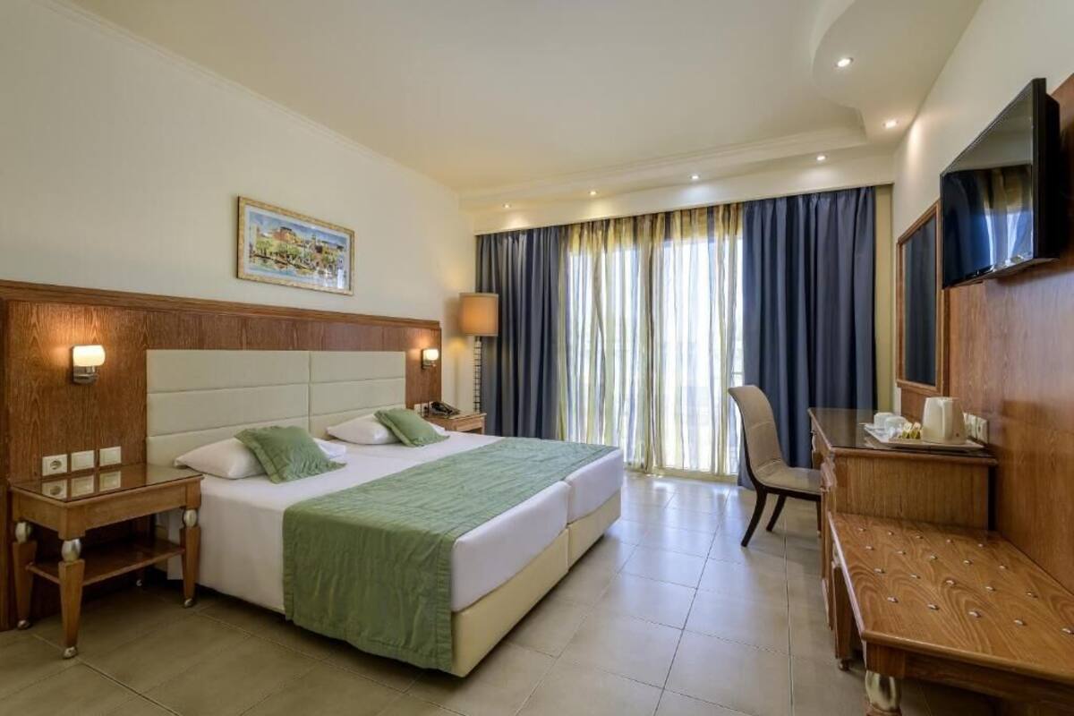 A hotel room with a large bed, a desk, a chair, a TV, and a window with curtains.